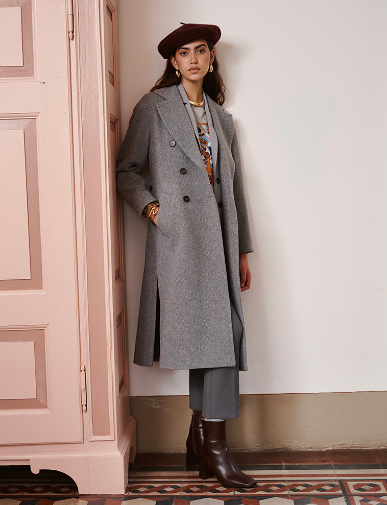 Modella indossa cappotto e pantaloni di colore grigio con stivaletti bordeaux.